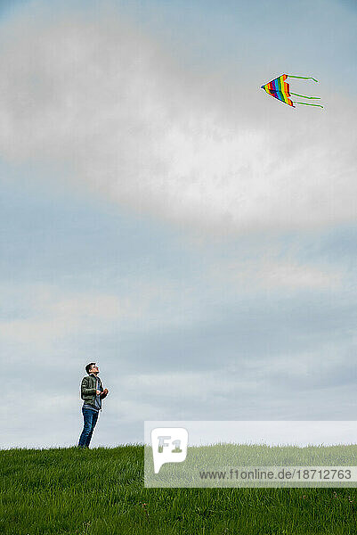Teenage boy flying a colorful kite alone on a cloudy day.
