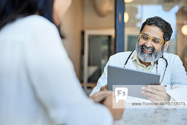 Happy male doctor using tablet PC sitting with female patient