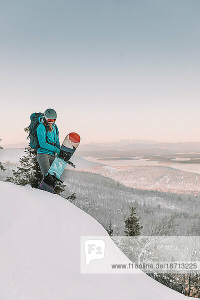 Woman with ski goggles and snowboard on mountain overlooking lake
