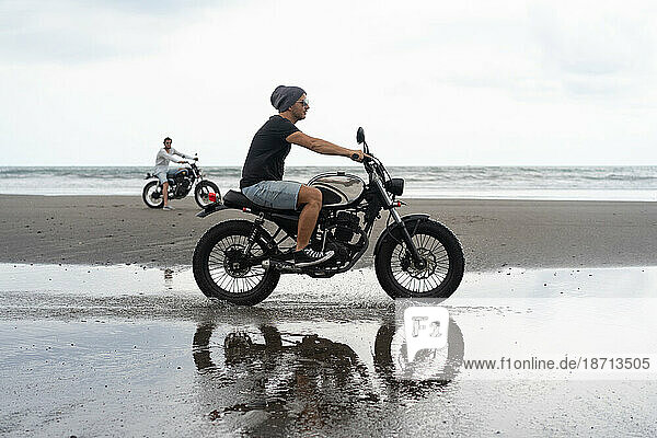 Young man riding a retro motorcycle on the beach.