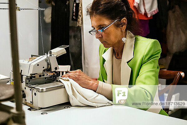 dressmaker woman sews with machine in her sewing workshop