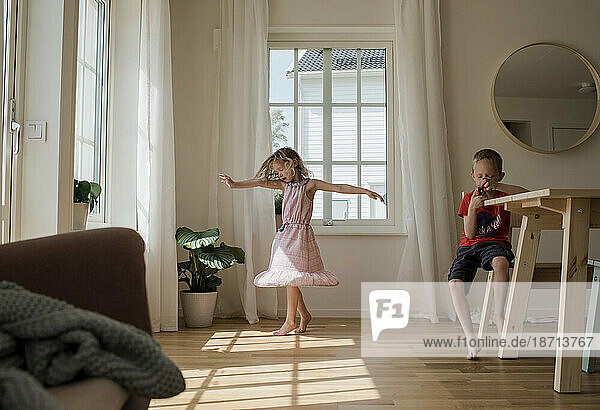 young girl dancing at home whilst her brother plays