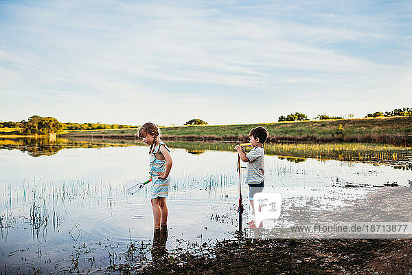 Young boy and girl standing at lake with fishing net and pole