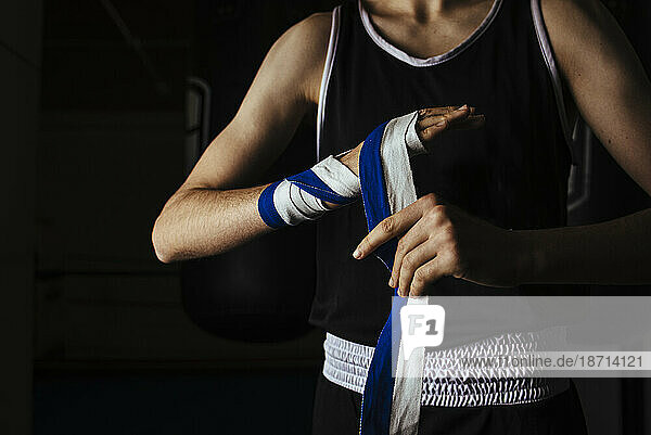 Young boxer placing hand bandages in gym before training.