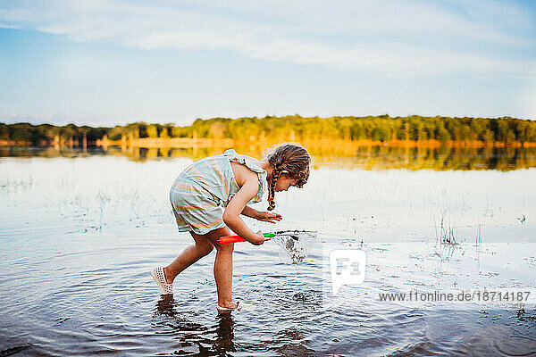 Young girl bending down to see fish in water at the lake