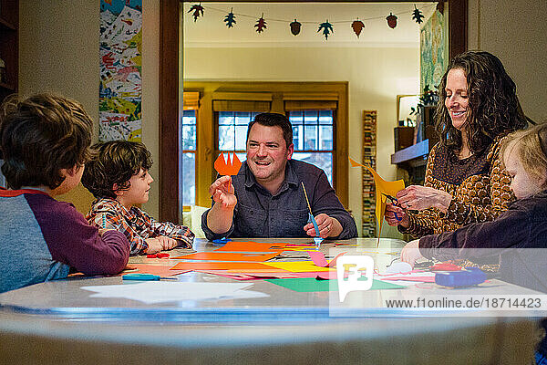 A smiling father sits at a table with his family creating paper crafts