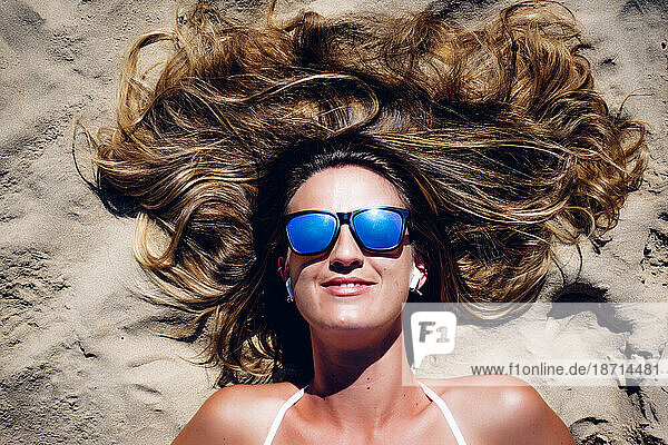 Close-up of blond woman with sunglasses lying on the beach sand.