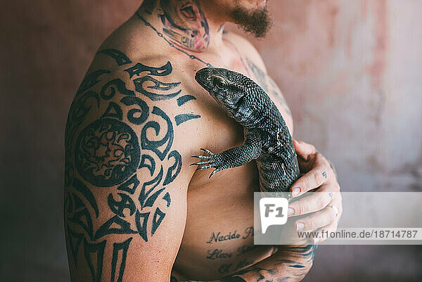 tattooed and shirtless man hugs a lizard Varanus exanthematicus