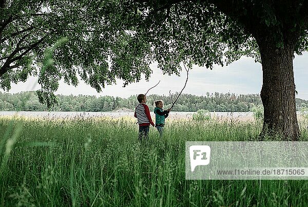 young boy and girl stood in a field playing with sticks