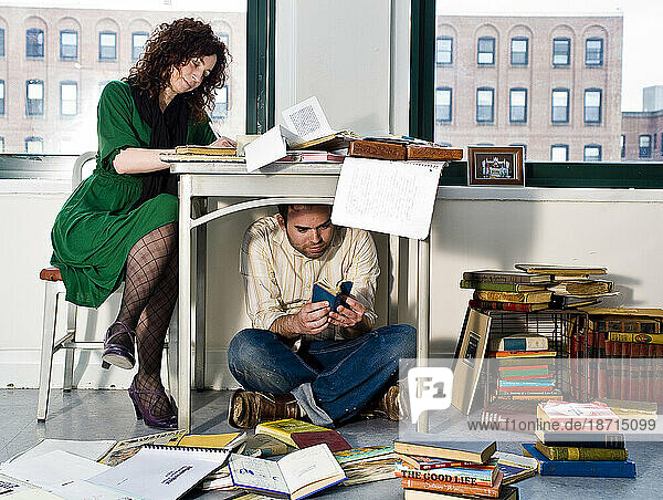 Young woman writing at desk & a man is under the desk