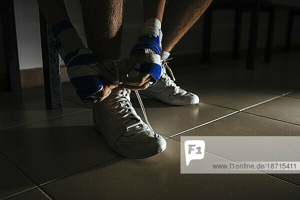 Closeup of boxer feet tying shoes before training in gym.