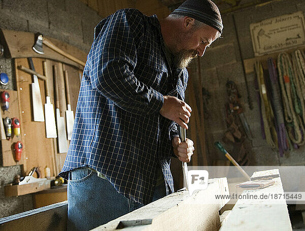 A timber framer uses a mortise chisel to clean out a mortise joint in his woodshop in Deforest  WI.