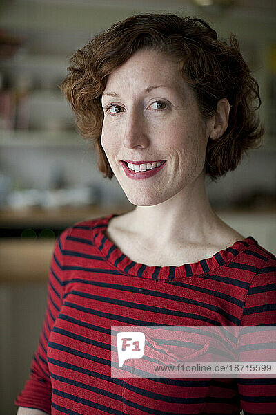 A redheaded woman wearing a red striped shirt smiles at the camera in her kitchen in Seattle  Washington.