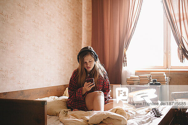 Teenage girl using smart phone while listening music on headphones