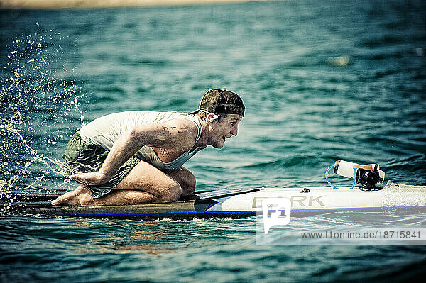 A close shot of a man on a paddleboard  racing off the coast.