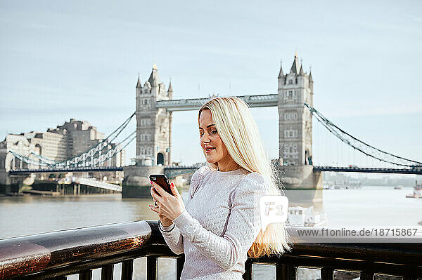 Attractive woman looking at mobile phone on background of Tower Bridge