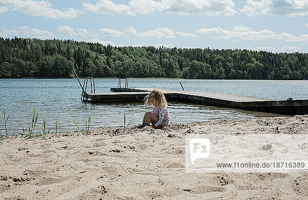 young girl sitting on a beach playing in the sand