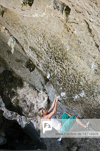 Female athlete hanging on for dear life as she works out a boulder problem in Thailand. Beautiful limestone rock with lots of nice holds.