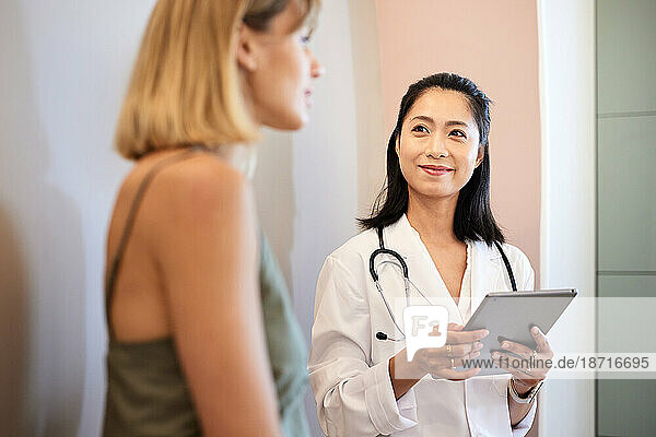 Smiling doctor holding tablet PC while listening to female patient