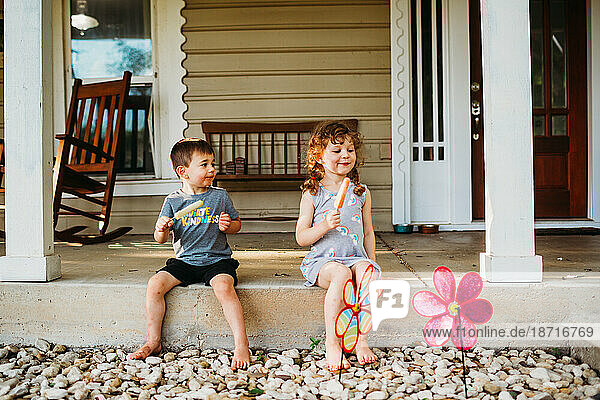 Young boy and girl sitting on front porch eating popsicles