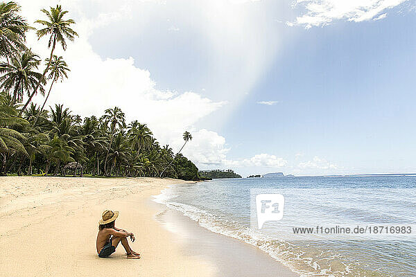 One man  wearing hat  relaxing at sandy tropical beach of Samoa