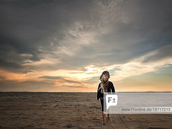 Young girl walking down sandy beach at sunset