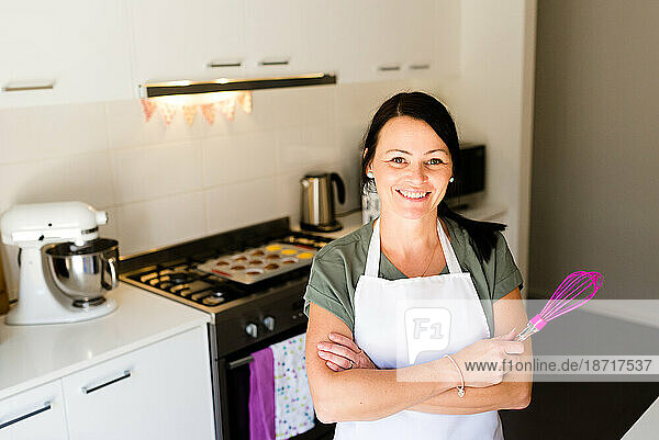 A smiling female baker in her kitchen holding a whisk