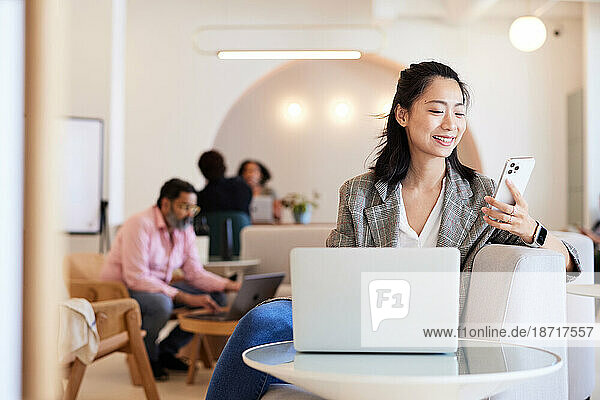 Smiling female entrepreneur using mobile phone sitting at cafe