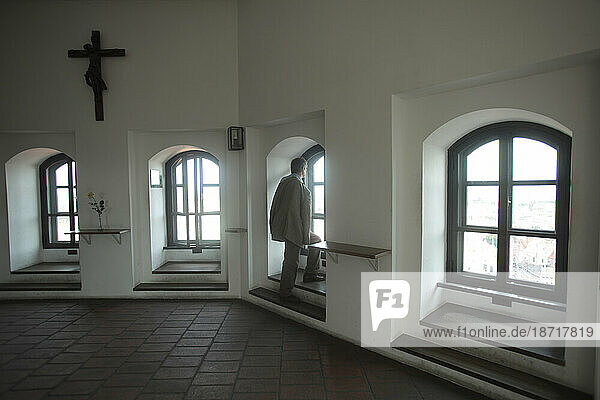 A man in a suit stands at a fill length window inside a church in Munich  Bavaria  Germany.