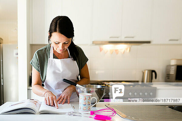 A female baker reading a cookbook while baking cupcakes