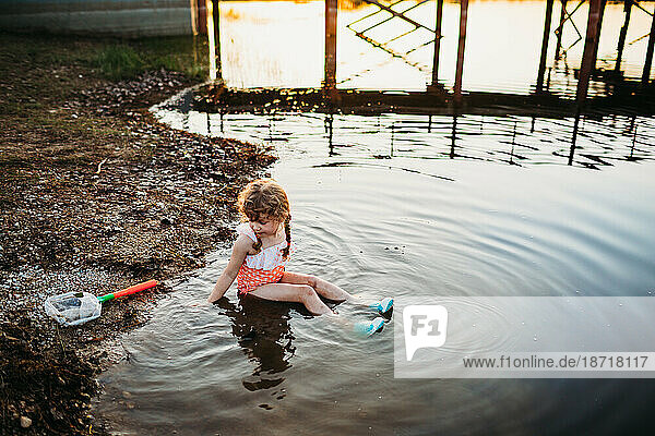 Young girl sitting in water at lake and catching fish with net