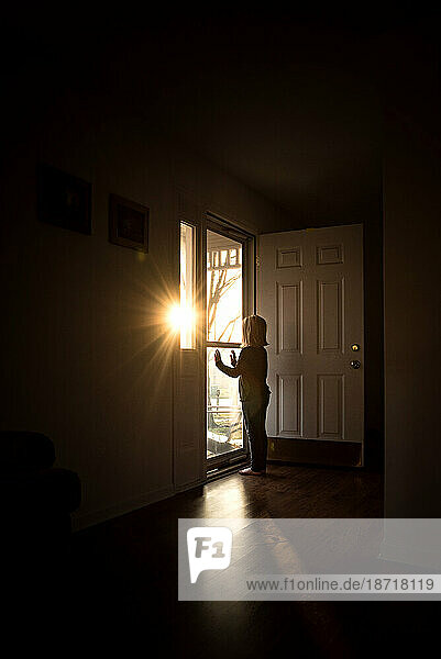 Young girl looking out door with sunshine