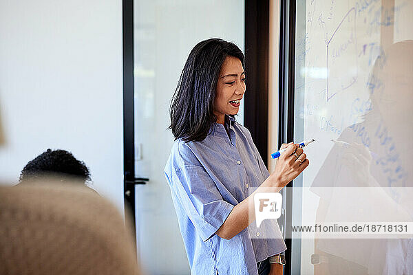 Smiling female entrepreneur writing on glass wall using felt tip pen