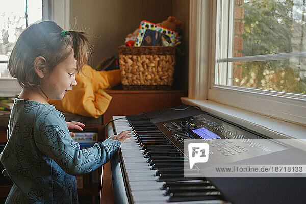 portrait of a cute little child playing piano in front of a window