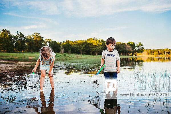 Young girl and boy looking into lake to catch fish with fishing net