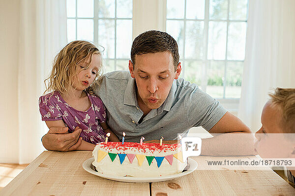 dad sat with his daughter and son blowing candles on a birthday cake