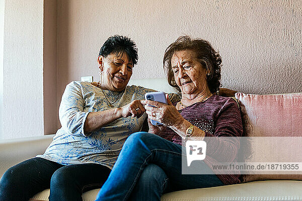 two old women looking at the smartphone sitting on the sofa