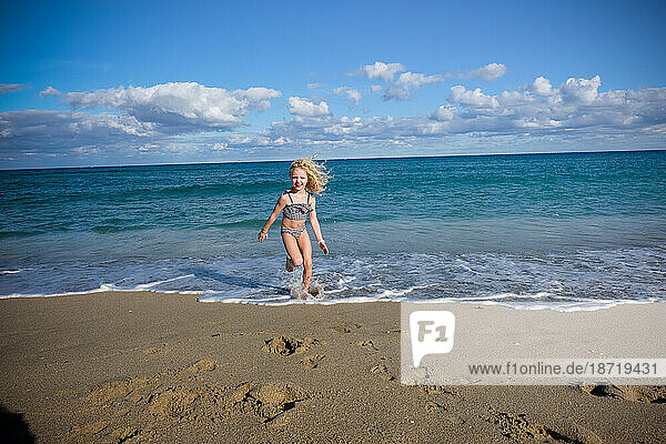 girl running away from ocean in bikini smiling on sunny day