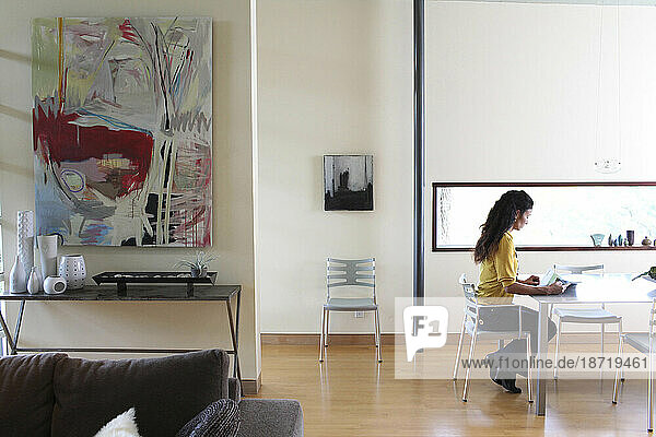 An Asian American woman sits in a chair and reads inside a modern home in Del Mar  California.