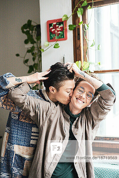 queer couple laugh at play in window light at home with plants