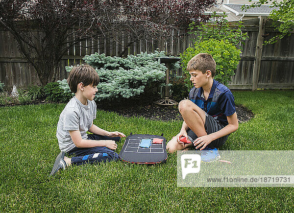 Two young boys playing a tic tac toe game in the backyard together.