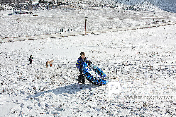 Boys and dog walking up sledding hill carrying snow tube