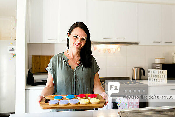 A smiling female baker displaying cookies in her kitchen