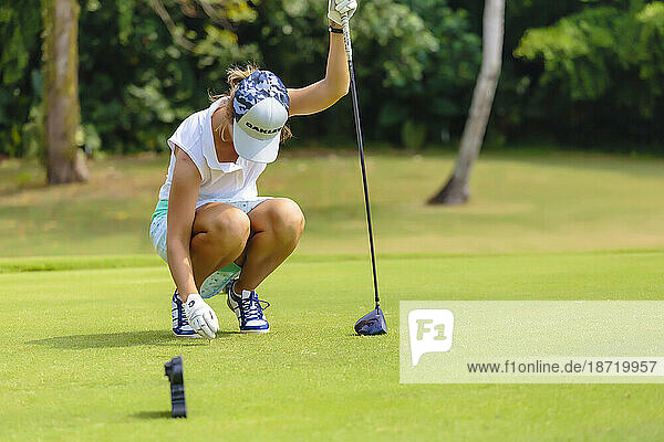 Full length of young woman placing golf ball on tee