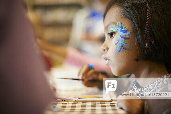 Cute little Asian girl in deep thought as she is painting in art class