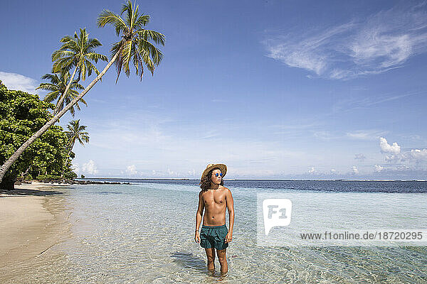 Tanned young man  at sandy beach of clear blue waters and palm trees