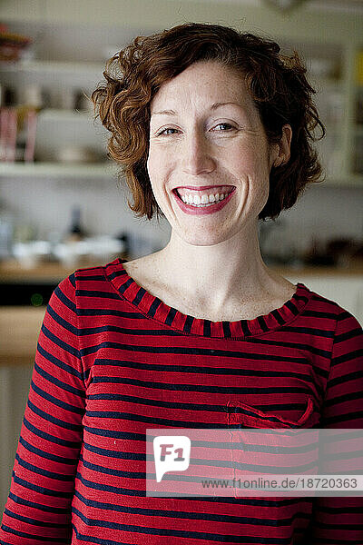 A redheaded woman wearing a red striped shirt smiles at the camera in her kitchen in Seattle  Washington.