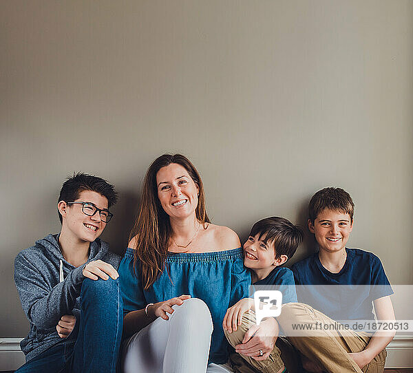 Mother and her three boys sitting on floor against a plain wall.