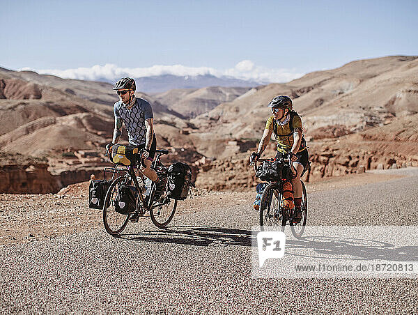 Two cyclists bike along remote mountain road in the desert of Morocco