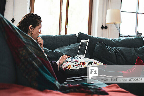 woman sits on cosy couch working from home on laptop device